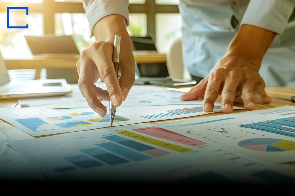 Person analyzing printed charts and graphs on a desk, representing data analysis and strategic planning, with Compunnel logo in the top left corner